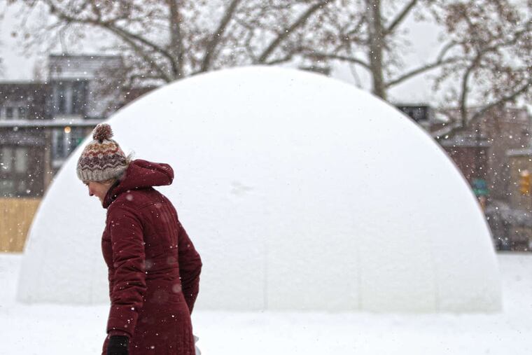 A pedestrian walks near the snow-covered "Winter Fountains" sculpture during a light snowfall Saturday on the Benjamin Franklin Parkway.