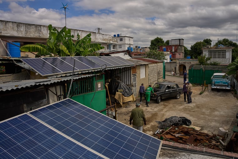 Solar panels cover the roof at the home of Felix Jose Morfi on Thursday while mechanics push his broken down Lada car in Regla, Havana province, Cuba.