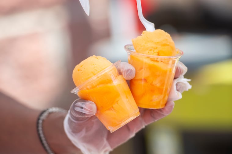 ODUNDE07-e.At Fred's Water Ice in Southwest Philadelphia two free cups of mango water ice are passed to a visitor on June 6, 2021. A scaled back Odunde festival kicked off this on Chester Avenue year in Southwest Philadelphia at FredÕs Water Icer. In years past the festival drew thousands to South St. The festival celebrates cultures and traditions of Africa and the African Diaspora throughout the world. This year, Odunde is being celebrated with 9 events from June 6th to June 13th. FredÕs Water Ice owner, Fred Cooper and his family gave out free water ice and soft pretzels to anyone who happened by his store. .(Jonathan Wilson / For the Inquirer)