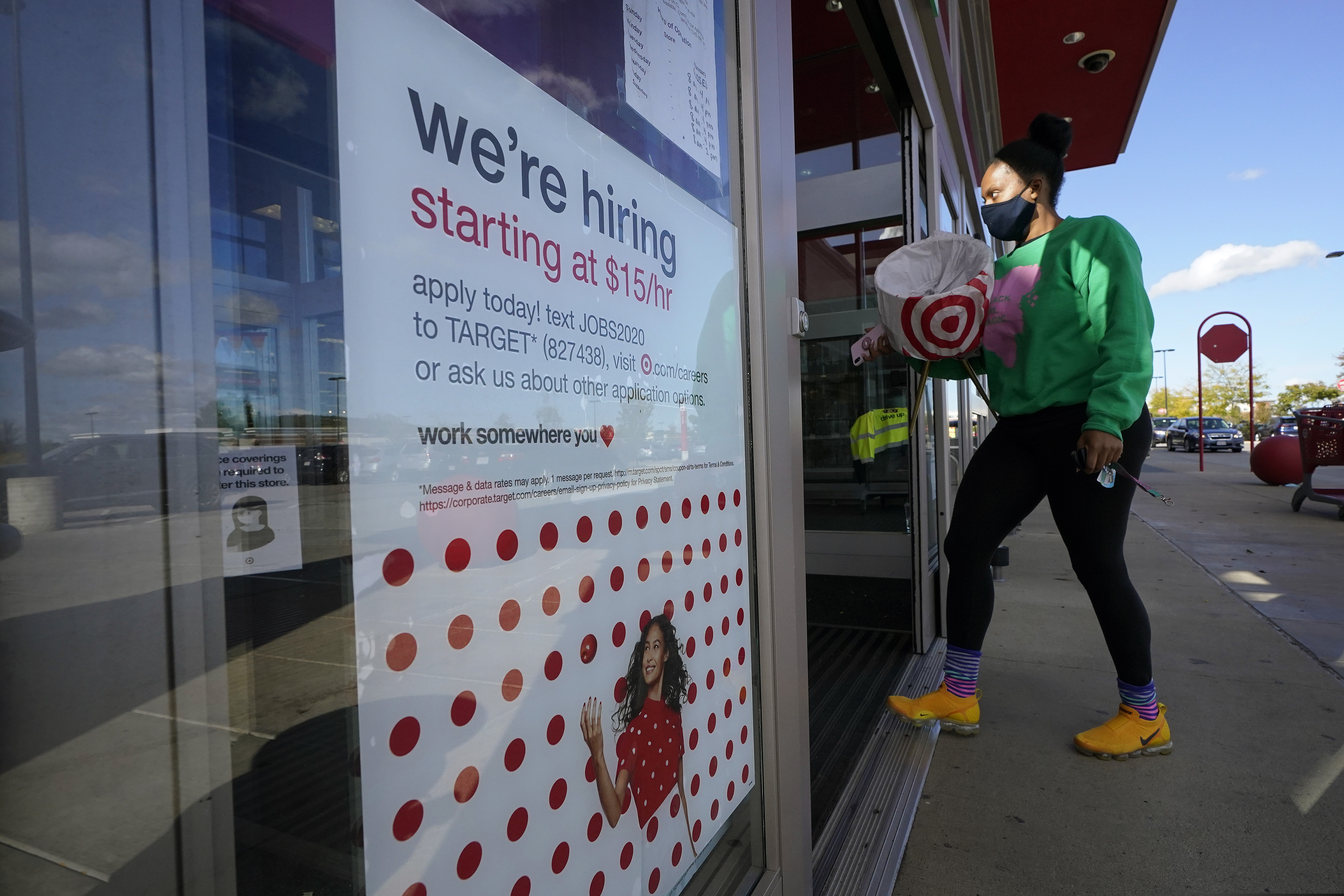 A passerby walks past a hiring sign while entering a Target store in Westwood, Mass. The number of Americans applying for unemployment benefits edged higher last week to 745,000, a sign that many employers continue to cut jobs despite a drop in confirmed viral infections and evidence that the overall economy is improving.