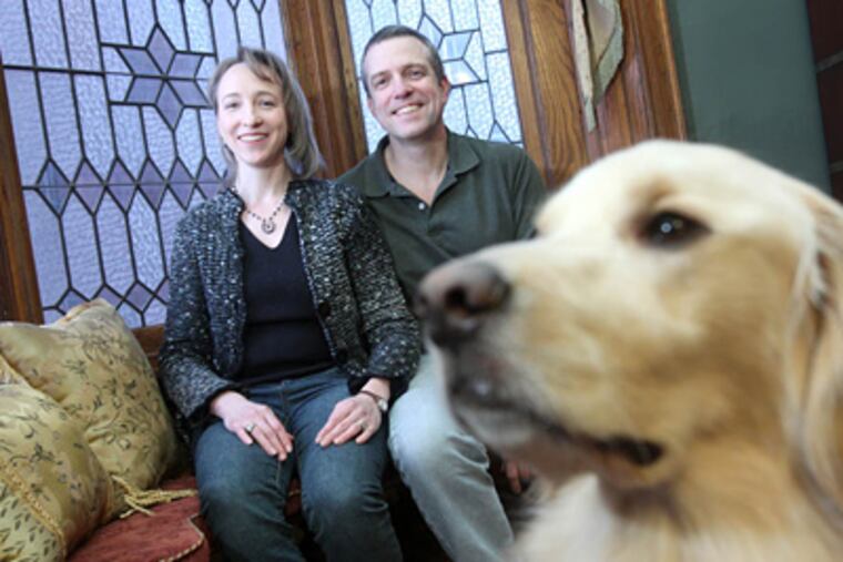 Nissa Blocher, left, and her husband, Victor Brubaker, sit on the first floor window seat in their West Philadelphia home. It was one of the features that attracted them to the home. In the foreground,is their dog, Jimmy. ( Charles Fox / Staff Photographer)