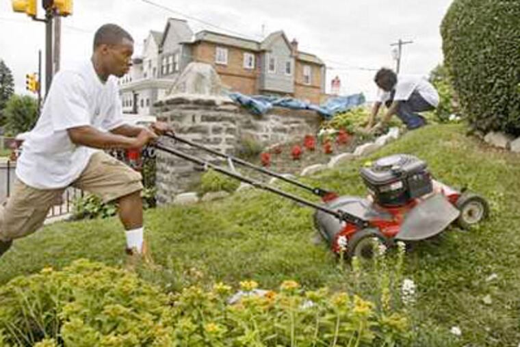 19-year-old old Khalif Moore (left) mows the lawn while Jaleel Buie, 17, weeds a flower bed in the 7000 block of Ogontz Ave in Phila. on June 23, 2009. ( Elizabeth Robertson / Staff Photographer )