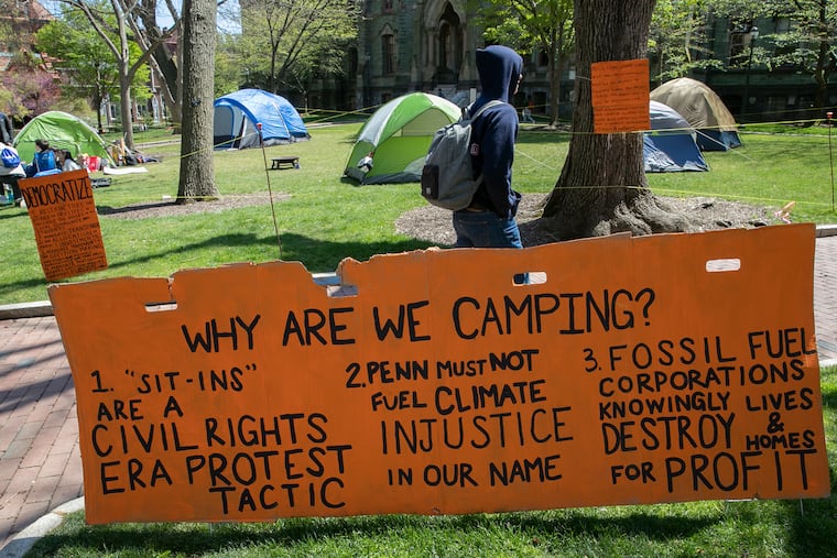 People walk past an encampment with signs by Fossil Free Penn at College Green on Penn’s campus in Philadelphia on Wednesday