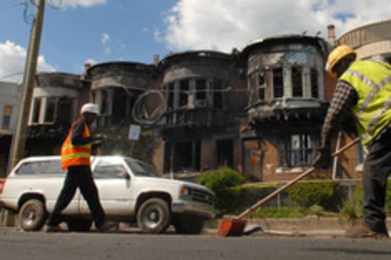 Workers clean up in front of four houses destroyed by fire at 58th Street and Cedar Avenue late Saturday. Three people were injured in the blaze, which has been labeled an arson. Fire investigators said that clothing and other items were ignited.