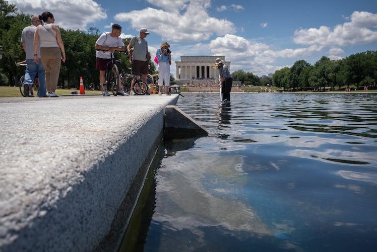 Visitors watch as a National Park Service employee uses a vacuum to clean the Lincoln Memorial Reflecting Pool near a missing section of blue coating, Friday, June 19, 2026, in Washington.