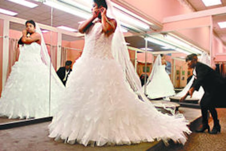 Aminah Heard puts on earrings while bridal consultant Aneesah Shareef adjusts her train. Heard was five months pregnant when she married last month.