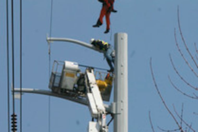A Coast Guard helicopter crew lifts a Peco worker to safety as another clings to a utility pole in Folcroft, where their cherry-picker failed.