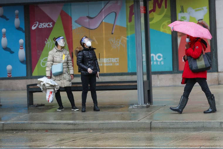 Pedestrians wait for the bus in the rain at 8th and Market Streets in Philadelphia, with signs promoting eating out, moviegoing, and shopping behind them on Friday, Dec. 04, 2020. Movie theaters are closed and indoor dining banned due to the spread of the coronavirus.