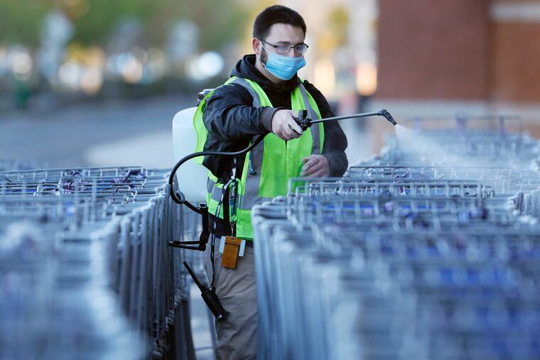 A worker sprays shopping carts with sanitizer at the Sam’s Club in Deptford.