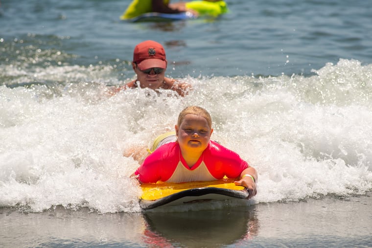 Lifeguard Ryan Comas, 20, of Philadelphia pushes Sage Praweckyj, 8, on her paddle board during the 11th annual 21 Down Beach Day at Schellenger Street beach in Wildwood. Every summer, the Wildwood Beach Patrol opens Lincoln Avenue Beach for kids with Down syndrome and their families for 21 Down Beach Day. On this day, these children swim with seasoned Wildwood lifeguards on soft-top paddleboards.