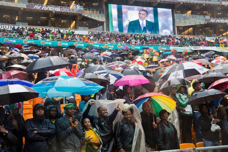 Spectators cheer amid an ocean of umbrellas as President Obama, shown on a big screen, speaks at the service. The rain was seen as a blessing by many. "Only great, great people are memorialized with it," said a South African.