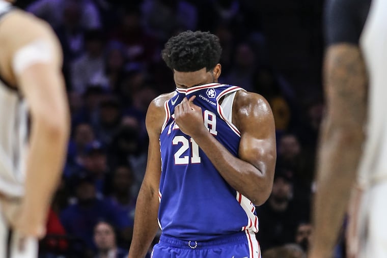 Sixers Joel Embiid wipes his face after colliding with the Nets' Nic Claxton during the 2nd quarter at the Wells Fargo Center in Philadelphia, Thursday, March 10, 2022.