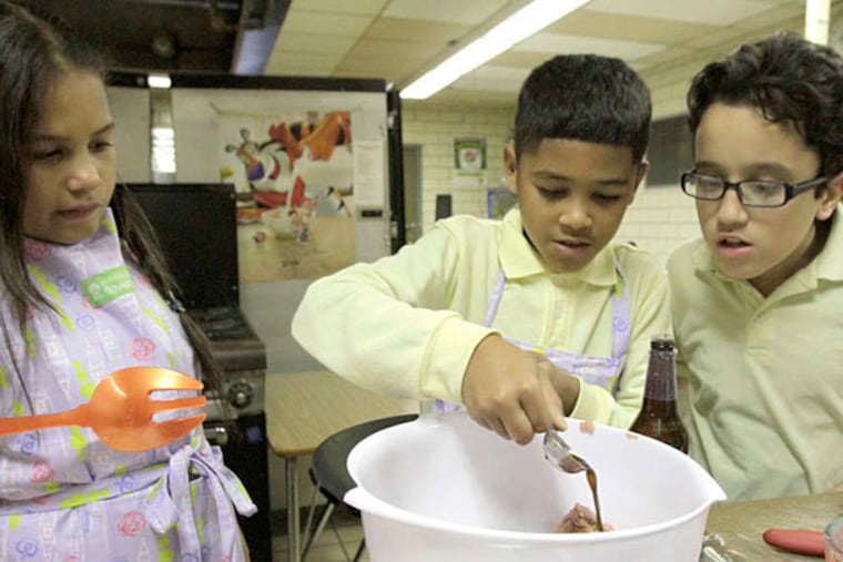 Learning to cook at Bayard Taylor school, Yariel Fernandez adds Worcestershire sauce to the turkey burgers as Lixjohanne Alicea and Mark Ramirez supervise. Eggplant fries were also on the menu.