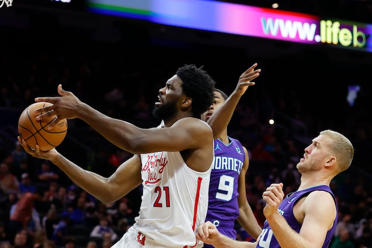 Sixers center Joel Embiid grabs the basketball past Charlotte Hornets guard Theo Maledon and center Mason Plumlee in the second quarter on Sunday, December 11, 2022 in Philadelphia.