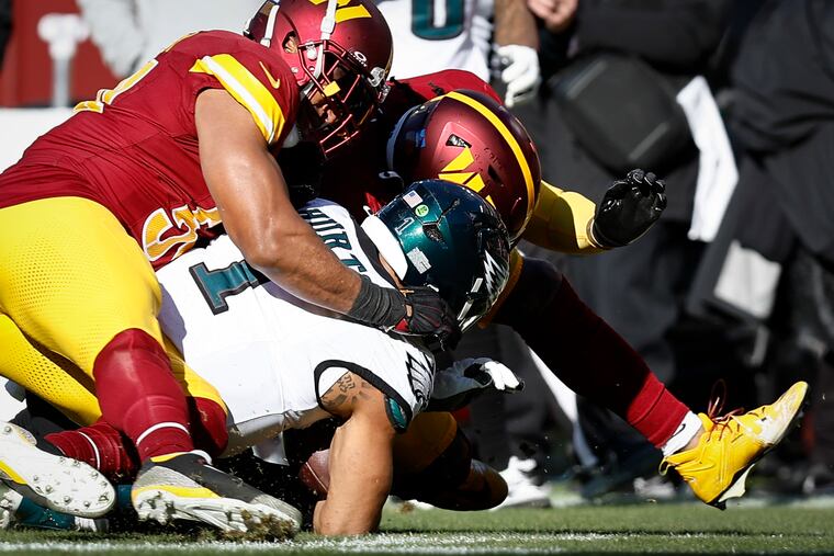 Eagles quarterback Jalen Hurts is tackled by Washington's Bobby Wagner and Frankie Luvu. Hurts left the game after this play.