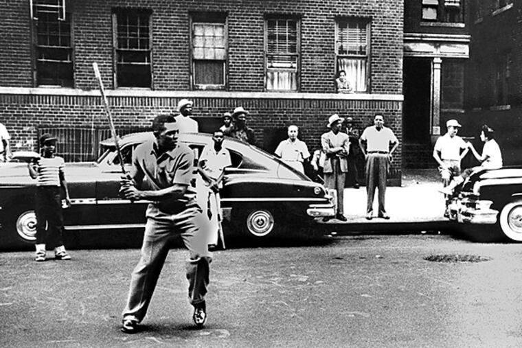 Full length action batting portrait of Hall of Famer, Willie Howard Mays in street clothes, playing stickball in Harlem, NY, c. 1950's with bystanders and tenements in background. (Handout photo)