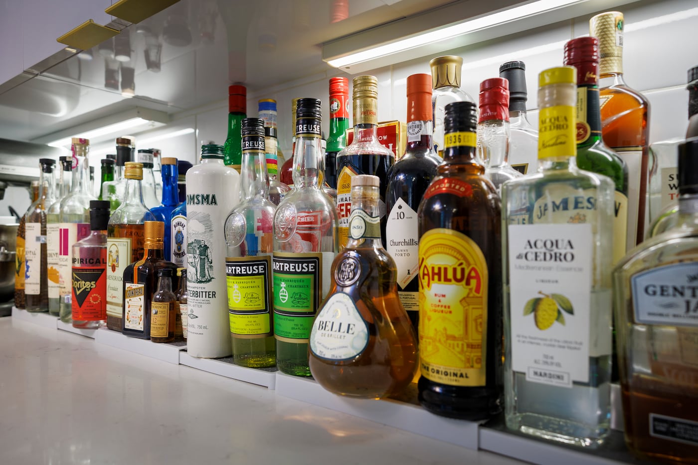 An eclectic and brightly colored mix of spirits line the kitchen counter, adding visual interest to the otherwise minimalistic kitchen.