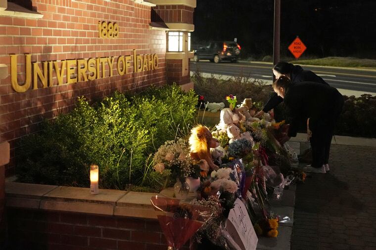 Two people place flowers at a growing memorial in front of a campus entrance sign for the University of Idaho on Nov. 16, 2022, in Moscow, Idaho.