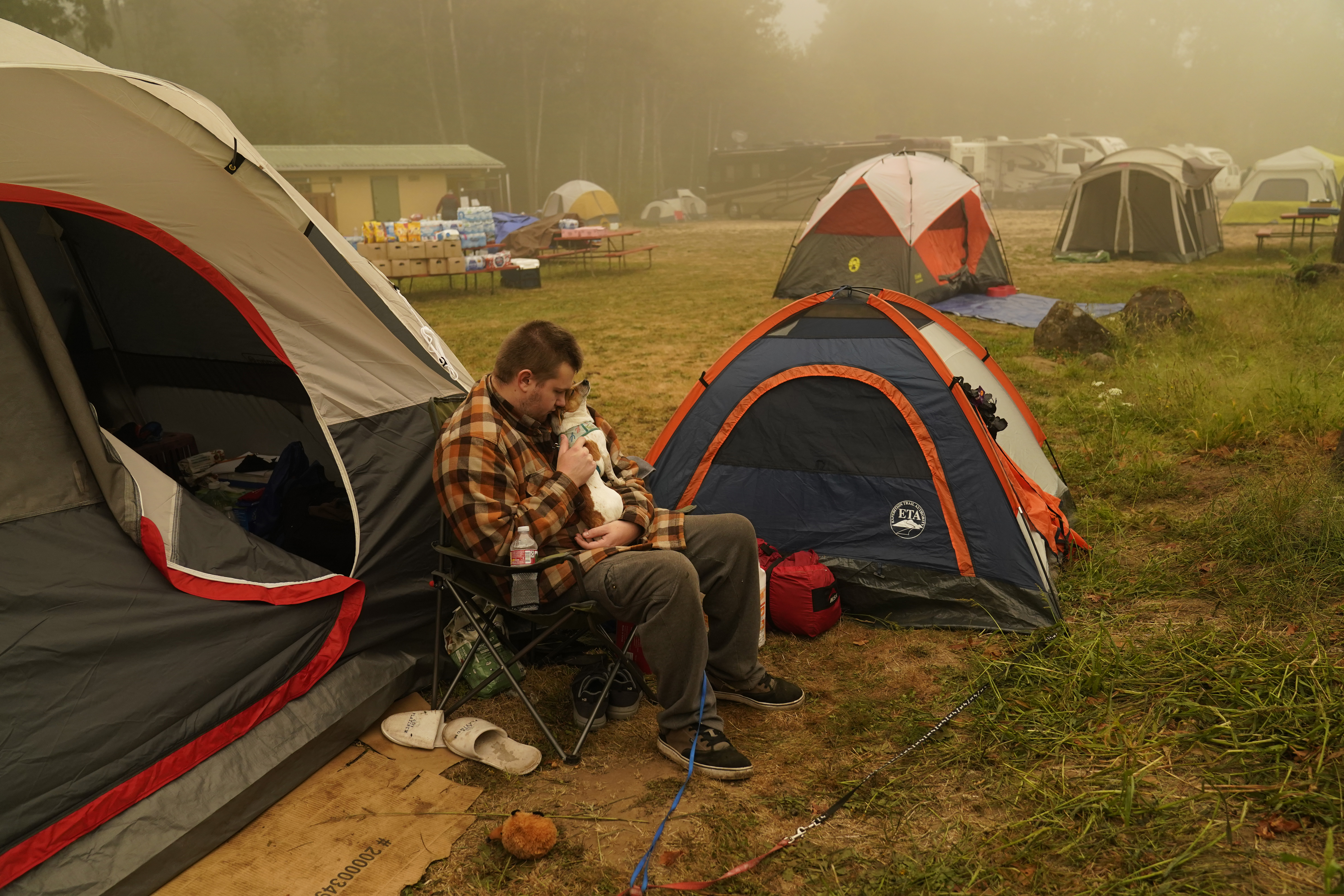 Kristopher Smith holds his dog Tripp outside his tent at an evacuation center at the Milwaukie-Portland Elks Lodge, Sunday, Sept. 13, 2020, in Oak Grove, Ore. Smith evacuated from Molalla, Oregon which was threatened by the Riverside Fire.