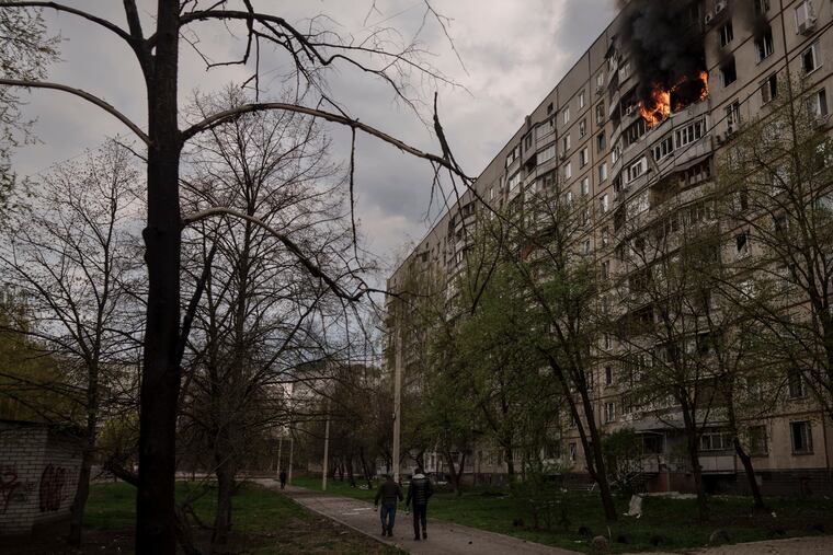 People walk near an apartment on fire after it was hit during a Russian bombardment in Kharkiv, Ukraine, Friday, April 22, 2022.