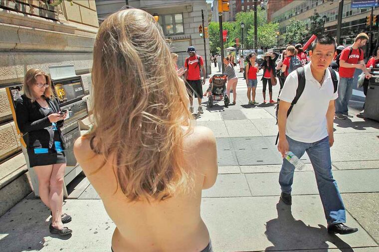 A seemingly confused man walks past Moira Johnston as she stands bared-breasted along Walnut Street near 18th on June 4, 2013. (ALEJANDRO A. ALVAREZ / STAFF PHOTOGRAPHER )