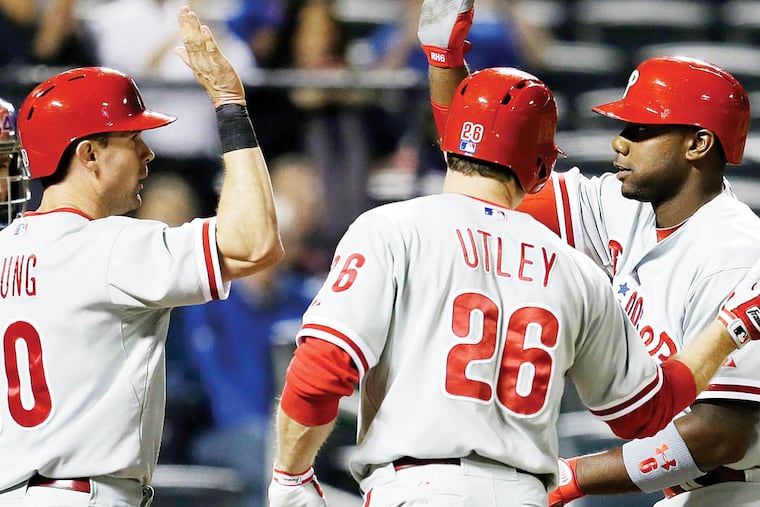 New York Mets catcher John Buck, left, watches as Philadelphia Phillies' Michael Young (10) and Chase Utley (26) greet teammate Ryan Howard at the plate after they scored on Howard's sixth-inning three-run home run off Mets starting pitcher Dillon Gee in a baseball game at Citi Field in New York, Friday, April 26, 2013. (AP Photo/Kathy Willens)