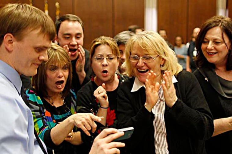 Chris Wurster (left) holds a phone for fellow workers at the Archdioscese of Philadelphia so they can watch a streaming video as the Pope is announced. Workers gathered in a room in the administration building to watch on a larger screen but the feed failed.