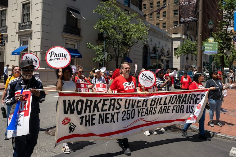 Employees at the downtown Sheraton Hotel represented by Unite Here Local 274, march through Center City Wednesday, after stopping at the Warwick Hotel Rittenhouse Square (rear). They walked off the job on June 21 demanding $30 per hour wages by 2028, additional healthcare resources, and other benefits that would put them on par with what other hotel workers have recently gotten in new union contracts.