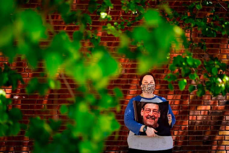 Sara Atkins poses for a photo in Wynnewood while holding a pillow with an image of her father, Andy Rotman-Zaid, who died of COVID-19 in December 2020.