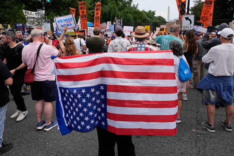 FILE - A demonstrator carries an American flag upside-down near the White House during a protest taking place on the day of a military parade commemorating the Army's 250th anniversary, coinciding with President Donald Trump's 79th birthday, June 14, 2025, in Washington.