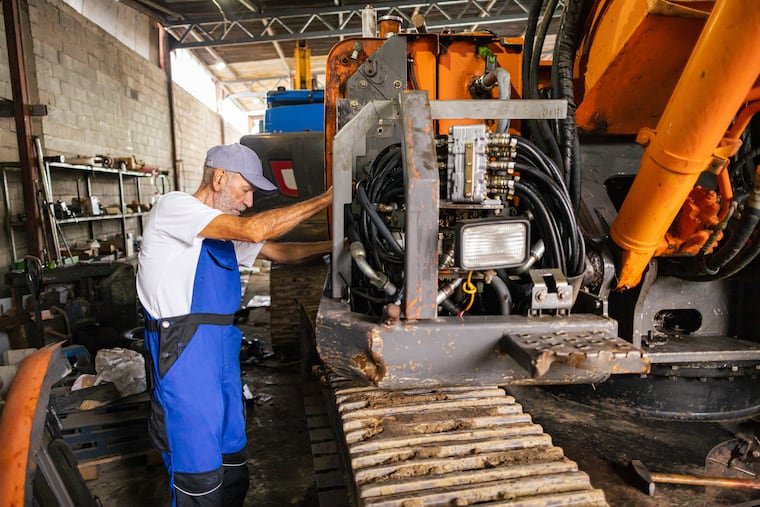 A skilled senior mechanic repairs an excavator in a garage, surrounded by tools and equipment.