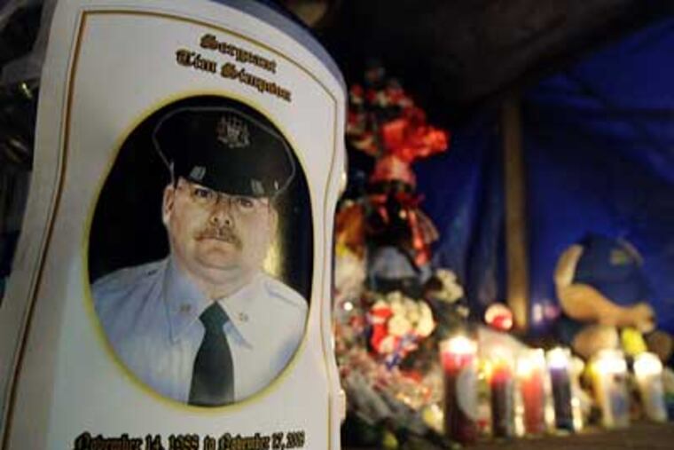A donation jug wrapped in a photo of Sgt. Timothy Simpson sits at a memorial for the fallen officer at Aramingo and Allegheny Avenues on Wednesday night. (Elizabeth Robertson / Inquirer)