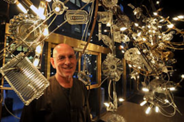 Lighting designer Warren Muller with the chandelier he created on Juniper Street. He recycles "what's available - found objects, trash."