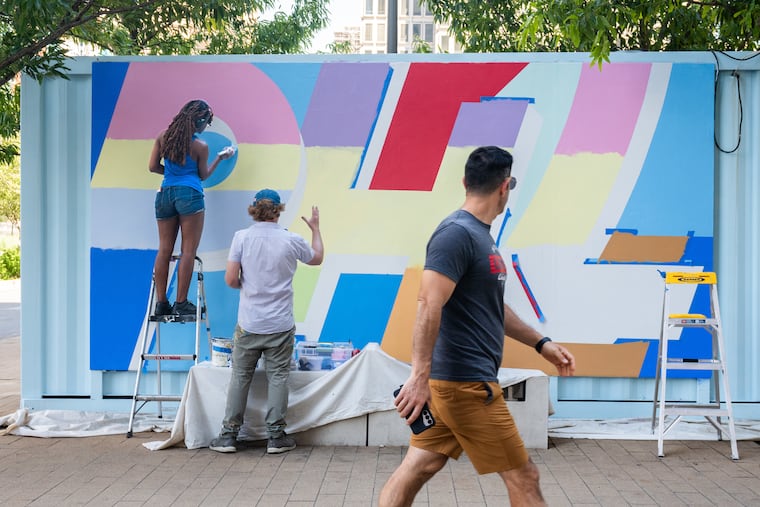 Artist Sanaa Webb, left, a rising senior at Arcadia University, and artist David Guinn, center, work on a Mural Arts Philadelphia mural in LOVE Park, June 24, 2026.
