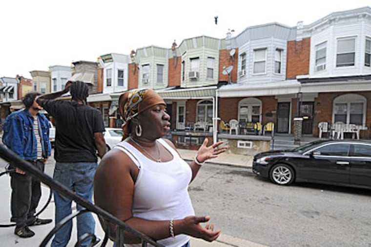 Neighbors, including Karen Mobley, congregate across the street from Corey White's family home (the one with the gold-colored chairs on the porch by her left hand) in the 5100 block of Webster Street, which is two blocks from where White was murdered overnight on Hadfield Street. (Clem Murray / Staff Photographer)