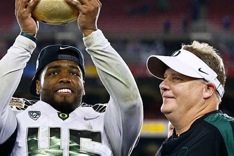Michael Clay, then an Oregon linebacker, now the Eagles' special teams coordinator, holds up the 2013 Fiesta Bowl trophy, with his mentor, coach Chip Kelly.