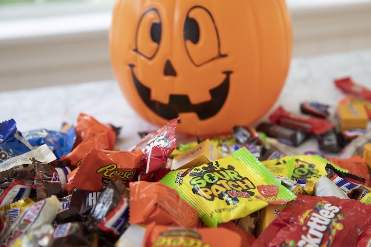 Chocolate and non-chocolate Halloween candy beside a pumpkin-shaped treat bucket.