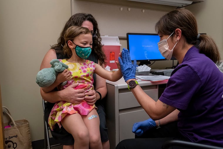 Nora Burlingame, 3, sits on the lap of her mother, Dina Burlingame, and gets a high five from nurse Luann Majeed after receiving her first dose of the Pfizer COVID-19 vaccination at UW Medical Center - Roosevelt on June 21, 2022, in Seattle. (David Ryder/Getty Images/TNS)