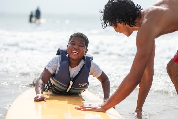 Jamir Price, 7, rides a wave with the help of Heart of Surfing's Dan Tracy during an event for kids with autism and developmental disabilities in Margate, N.J. This was Price’s first time ever surfing and attending the event.