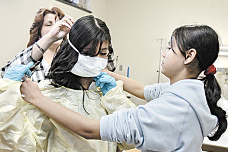 Dalia Perez, 14 (center ) gets help in putting on a gown and a mask from student service coordinator & RN, Deborah Molone and fellow student, Justine LaBoy,13 during visit to Helene Fuld School of Nursing building. (Akira Suwa / Inquirer )