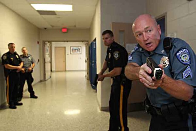 With his empty gun drawn, Sargent William Moyer, right, looks down the school hallway acting as support to the two other police officers that are in the classroom behind him looking for the shooter or wounded during a training exercise at Spring-Ford High School. Local popilce were being trained byt eh Montgomery and Chester Counties SWAT teasm. Police team up with Montco school district for a workshop on how to respond to an active-shooter situation. Teachers and first responders will run through drills and scenarios at Spring-Ford High in Royersford, PA 06/25/2013 ( MICHAEL BRYANT / Staff Photographer )