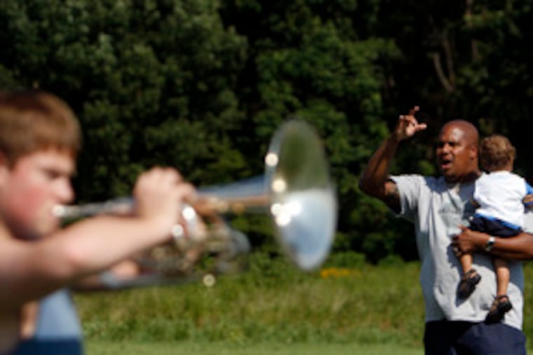 Deptford High School assistant band director Calvin Spencer conducts rehearsal at a minicamp at the high school with his son, Dante, 15 months old.