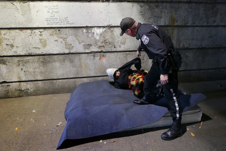 A Philadelphia police officer wakes up a homeless man as workers perform a weekly cleanup under a Kensington bridge. Workers had called police to wake the man up. After several attempts, the man got up.