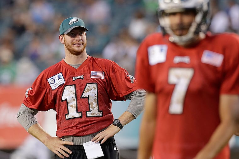 Carson Wentz watches practice as Sam Bradford walks in front at Lincoln Financial Field.