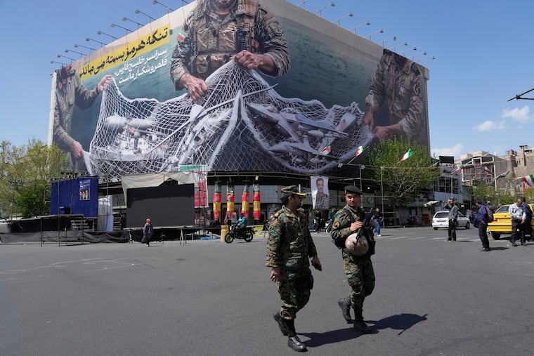 Two police officers walk in front of an anti-U.S. billboard depicting the American aircrafts into the Iranian armed forces' fishing net with signs that read in Farsi: "The Strait of Hormuz will remain closed. The entire Persian Gulf is our hunting ground," at the Eqelab-e-Eslami, or Islamic Revolution square, in downtown Tehran, Iran, Sunday.