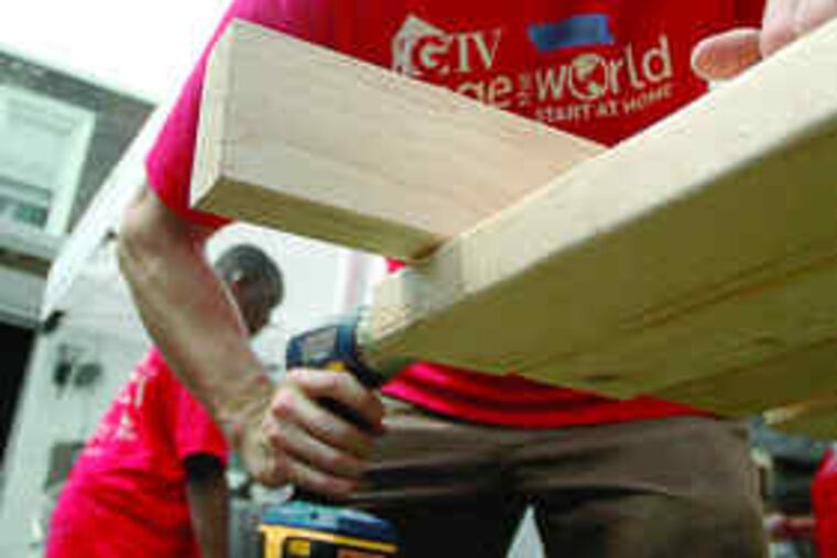 VOLUNTEERING with HGTV's "Change the World," a carpenter (above) yesterday helps renovate a 70-year-old Frankford rowhouse chosen for a makeover by the host, Carter Oosterhouse (right, chatting with another red-shirted volunteer). The facility, on the 4200 block of Romain Street, provides transitional housing for veterans.