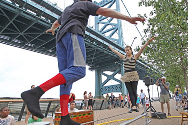 David Gillies (left) and Erica Saben work on their wire act as the Give and Take Jugglers get warmed up before their performance at The Race Street Pier. ( Michael Bryant / Staff Photographer )