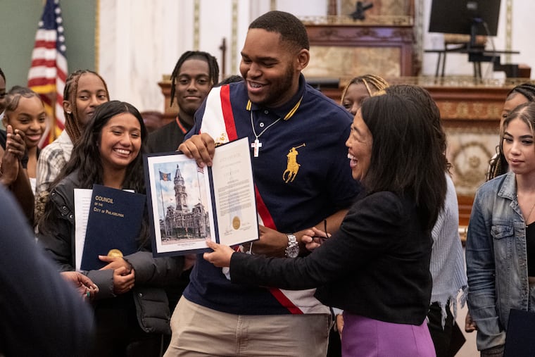 George Washington HS cheer team, Roland Williams, smiles as he receives his honorary certificates from Council Member Helen Gym, right, at the Philadelphia City Hall chambers. The team was honored with a resolution celebrating them being the first Philly team to make it to nationals.