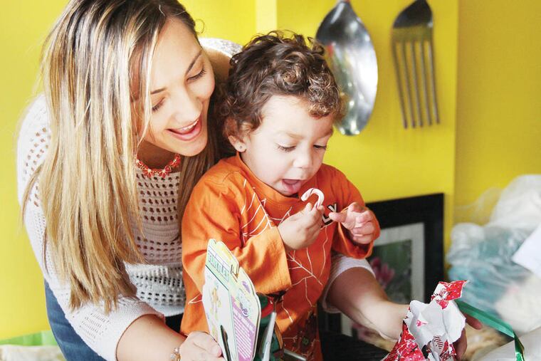 Mandi Cruz, left, who works at the Camden Covenant House, helps Jonathan Roque, 1, open a present during a Christmas party for the Covenant House at the Reggae Grill in Camden, NJ on December 18, 2014. ( DAVID MAIALETTI / Staff Photographer )