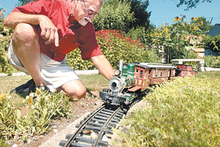 Mark Driver makes adjustments to the replica of a coal fire steam engine that runs an oval around the central garden in his back yard. (Ron Tarver / Inquirer)